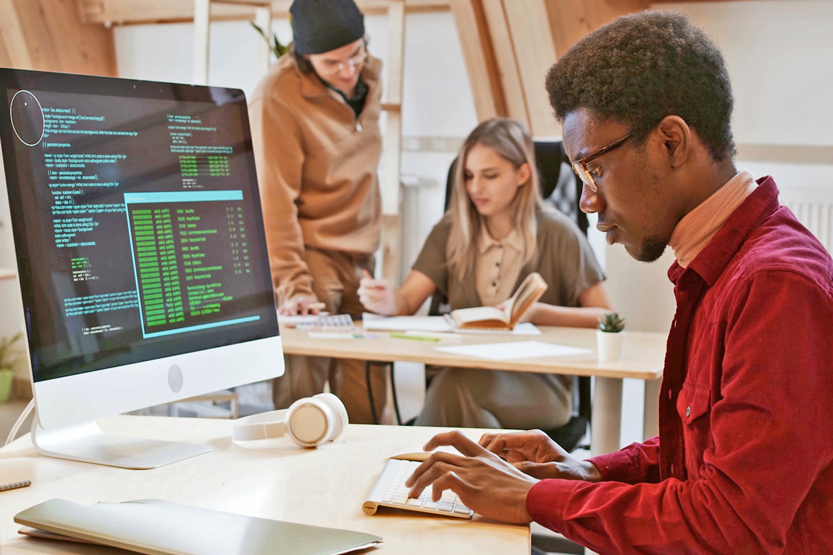 Man using a computer to write codes while coworkers chat in the background