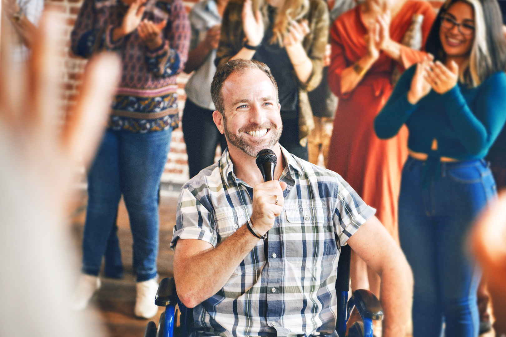 smiling keynote speaker in a wheelchair holding a microphone while getting cheered on by his peers