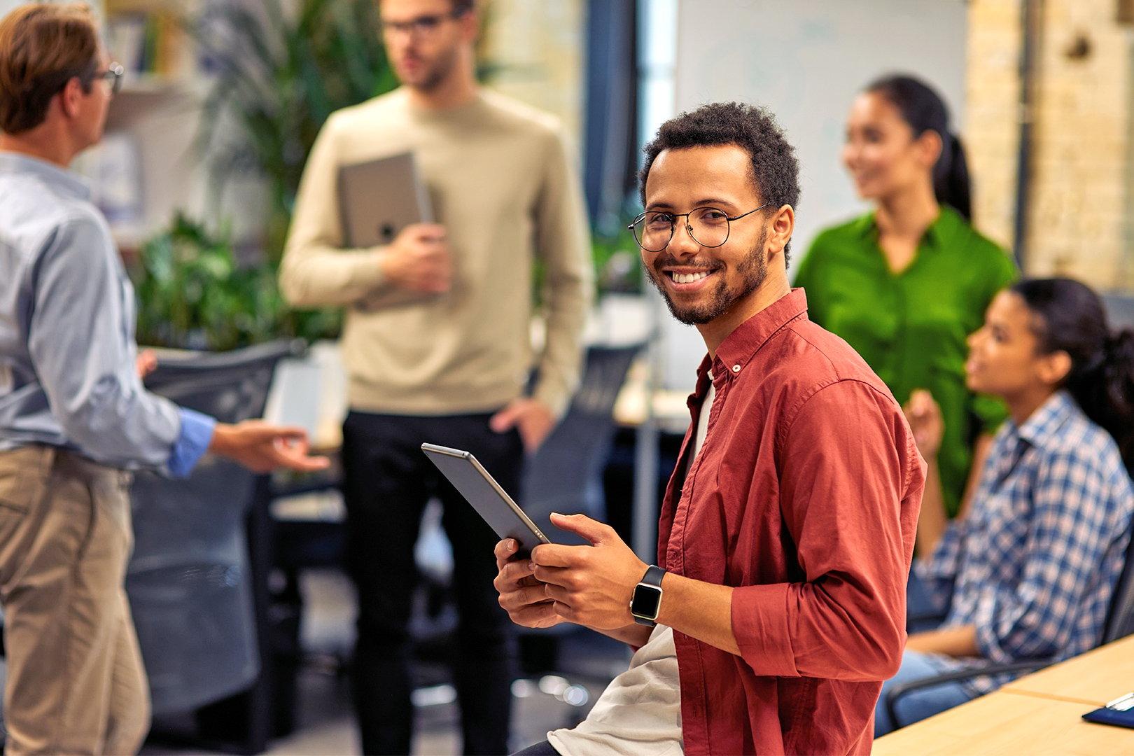 Young african american man holding a tablet while his coworkers chat in the background