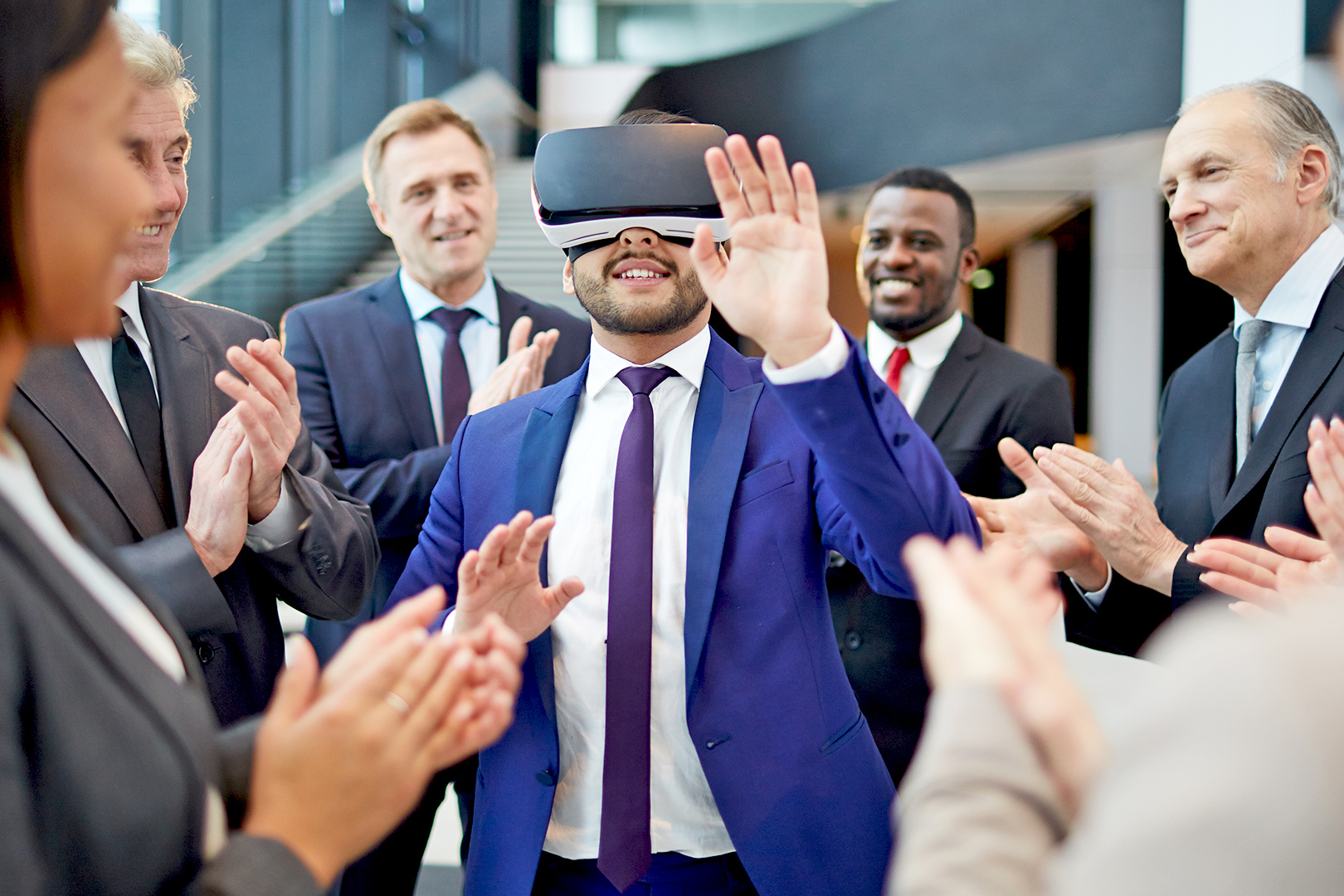 Man with virtual reality headset with other people in suits around him clapping