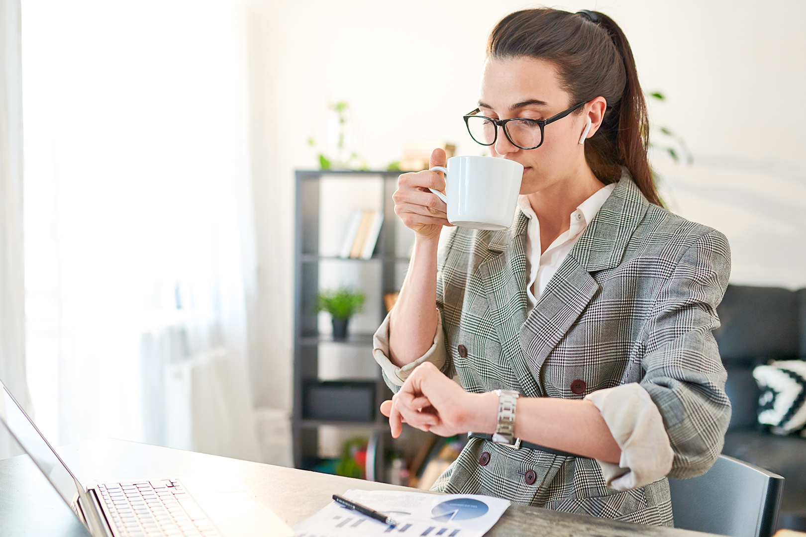 Caucasian woman drinking a hot beverage while working at the time in her wrist watch