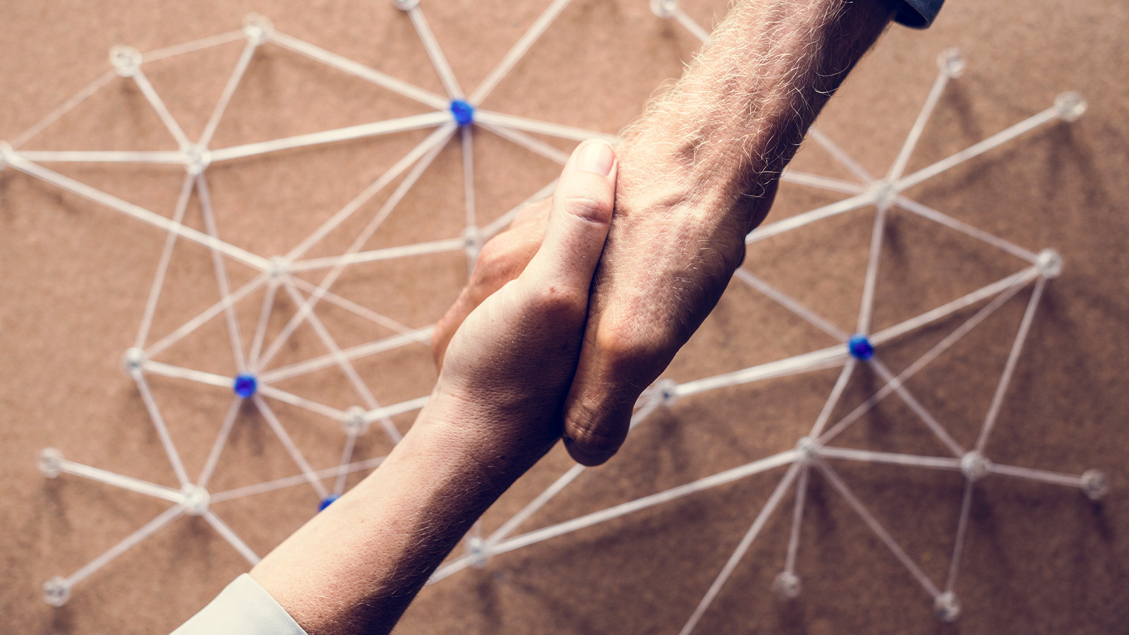 Two people shake hands in front of a network-like web of strings and nodes, symbolizing connection, trust, and the power of networking.
