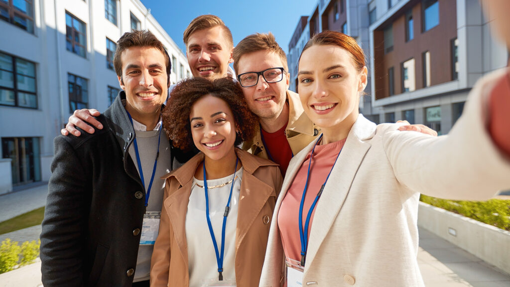 A diverse group of young professionals smiling together outdoors, capturing a friendly moment that reflects connection, belonging, and a strong sense of community.