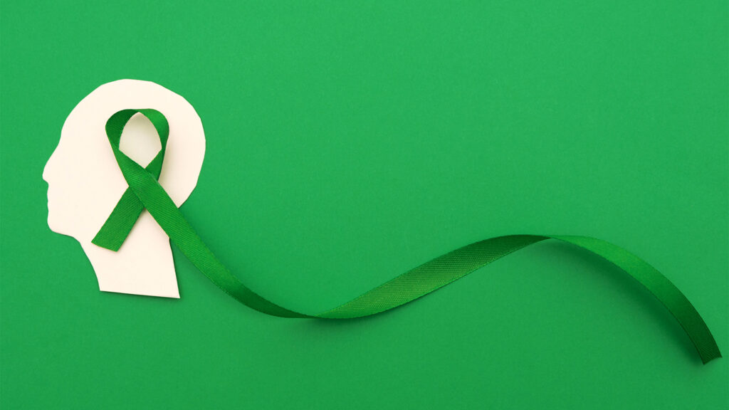 A paper cutout of a human head with a green mental health awareness ribbon on a green background, symbolizing anxiety awareness.