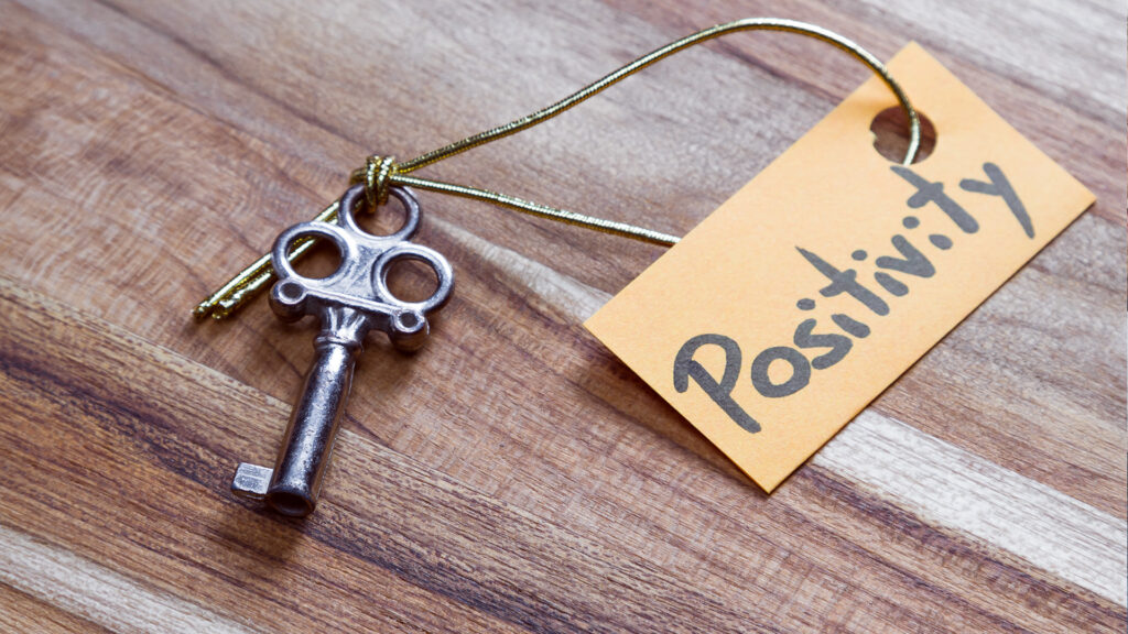 A vintage key attached to an orange tag labeled "Positivity" resting on a wooden surface.