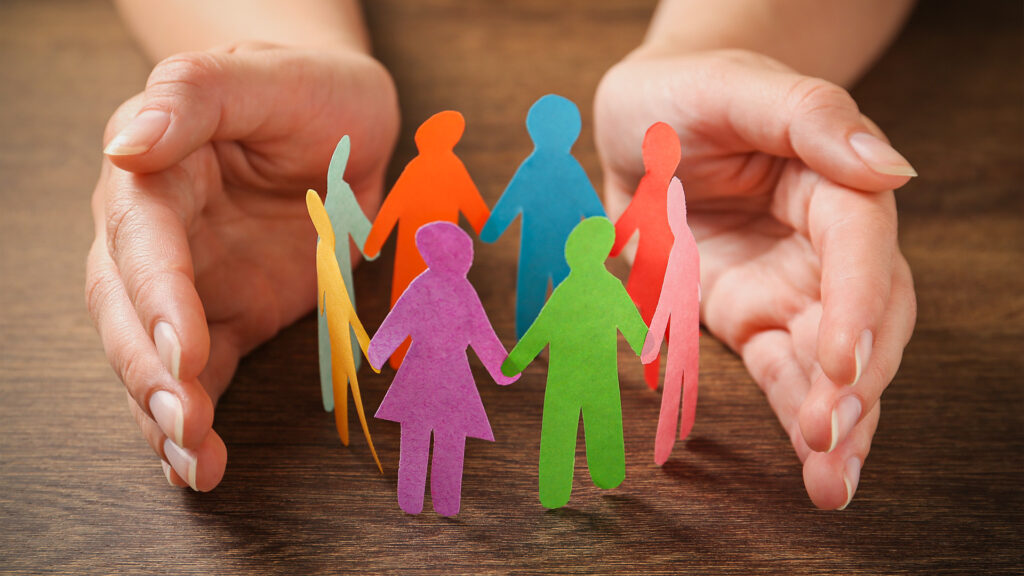Two hands cup around a circle of colorful paper people to represent psychological safety at work.