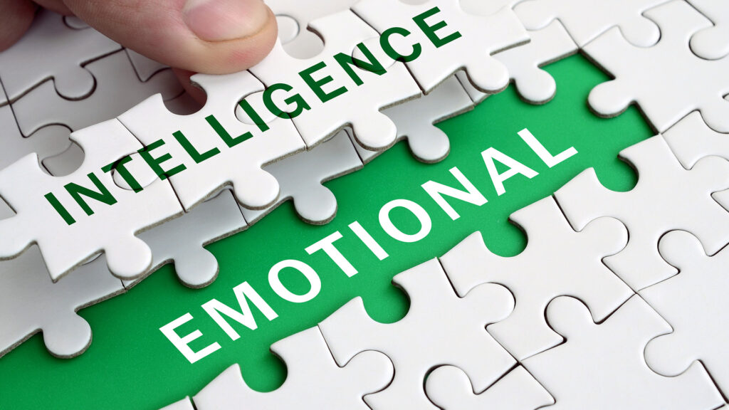 A hand placing a puzzle piece to reveal the words "Emotional Intelligence" on a green background beneath white puzzle pieces.