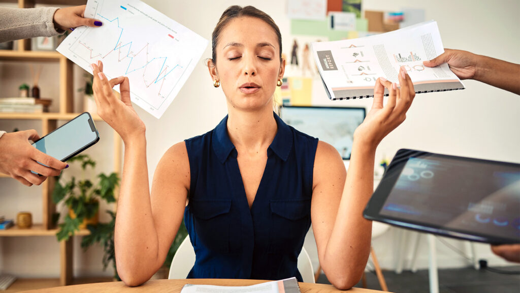 A woman sitting calmly with eyes closed as multiple hands around her reach in with phones, reports, and tablets, illustrating the overwhelm of workplace productivity demands.