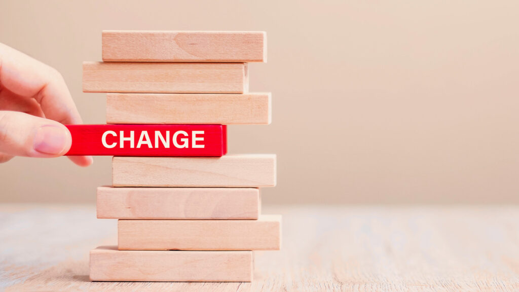 A hand pulls a red block with the word change on it from a stack of wooden blocks.