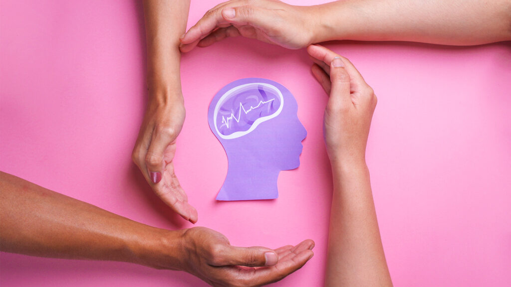Three people use their hands to form a circle around a paper head to show psychological safety.