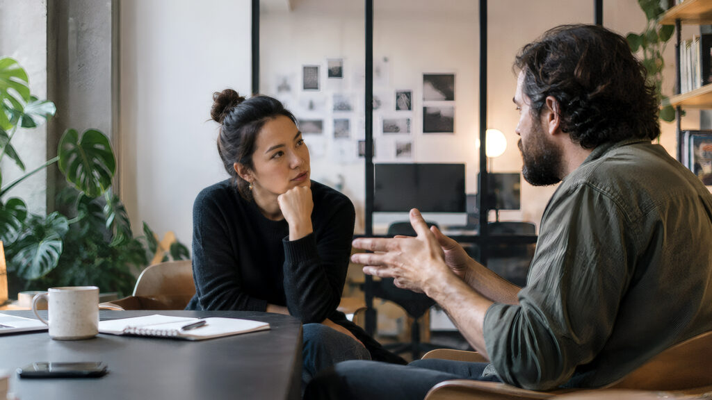 A woman rests her chin on her hand and listens to a man talk during a work negotiation.